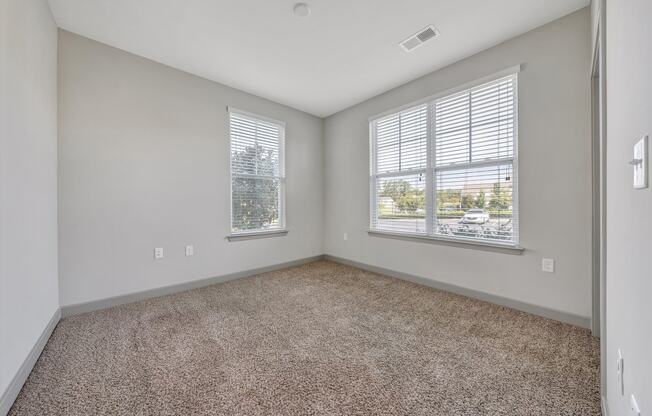 an empty living room with two windows and carpeting