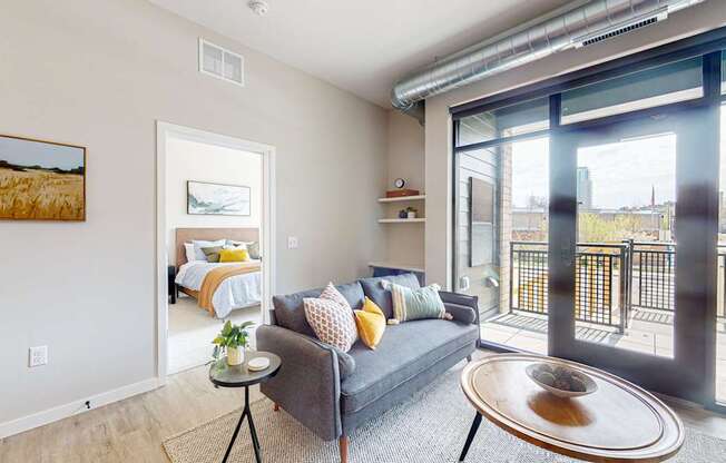 a living area with a couch coffee table and sliding glass door to a bedroom with a bed