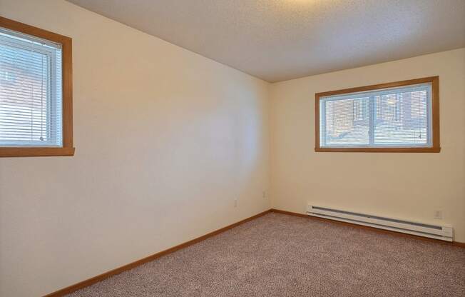 a bedroom with two windows and carpeted floors. Fargo, ND Dakota Manor Apartments