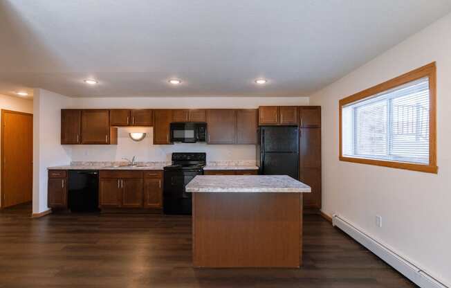 a kitchen with black appliances and an island with a window. Fargo, ND Westwood Apartments