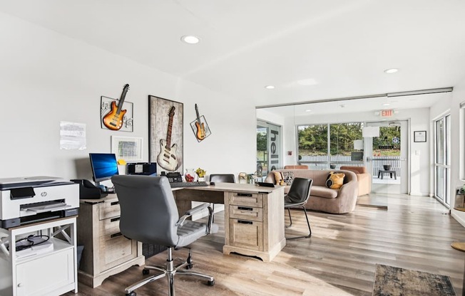 A room with a desk, chairs, and guitars hanging on the wall.