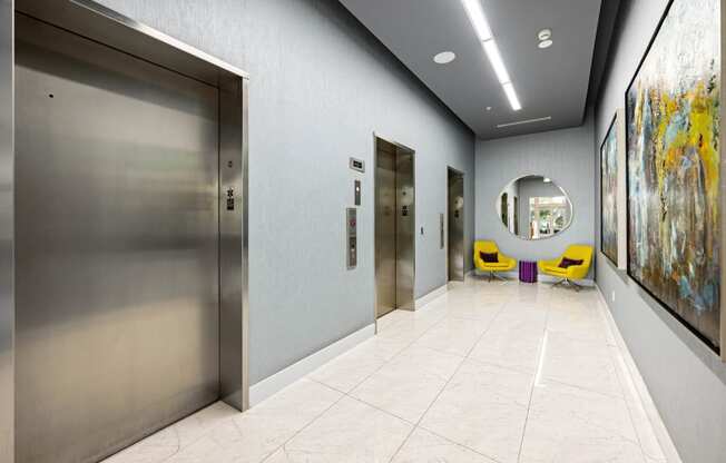 a hallway with elevators and a large painting on the wall and yellow chairs