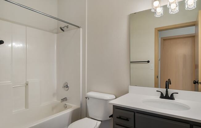 a full bathroom with a vanity sink, white countertops, cabinet storage, a toilet and the shower and bathtub.at Shoreline Village, Washington