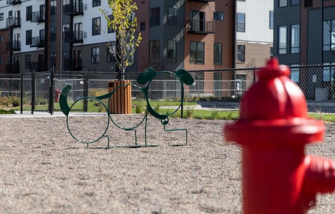 A red fire hydrant is in the foreground of a playground with a green swing set.