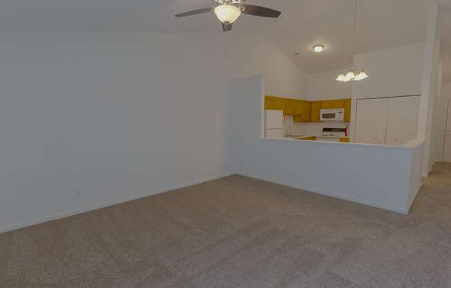 an empty living room with a ceiling fan and a kitchen
