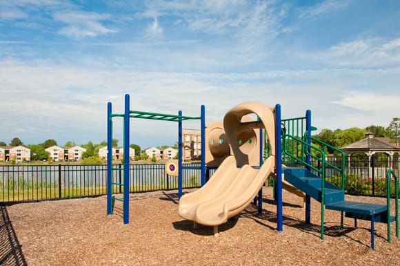 Playground with slide, monkey bars and steps; surrounded by a fence; overlooking community lake