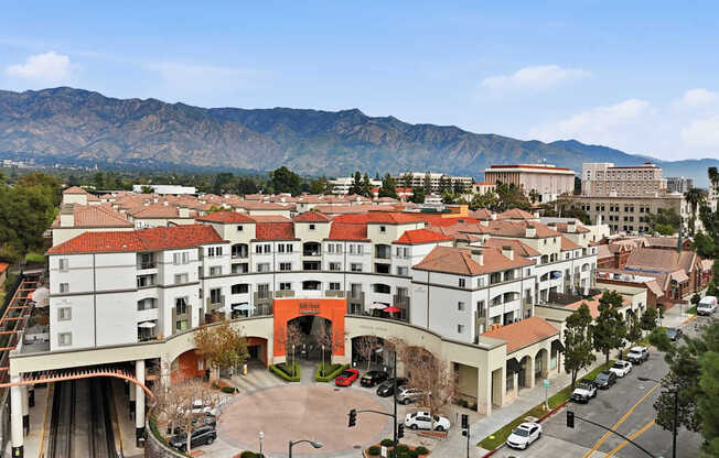 A large white building with a red roof is surrounded by mountains.