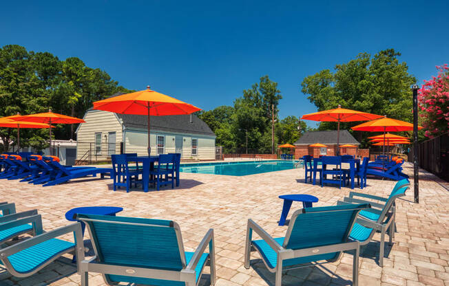 a pool and patio with blue chairs and umbrellas