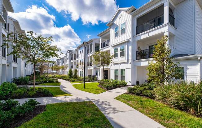 A row of white townhouses with a sidewalk in front.