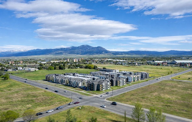 A large building complex is surrounded by a grassy area and a road with cars.