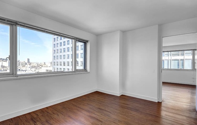 an empty bedroom with a large window and hardwood floors