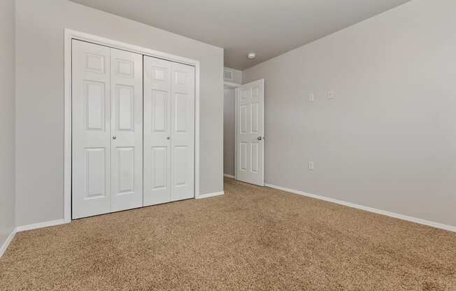 A room with carpeted floor and white walls with a white door and a white wardrobe with four doors.
