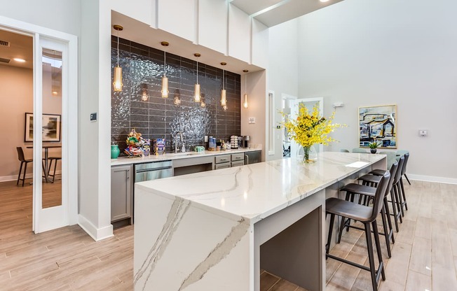 a kitchen with a large white island with a long countertop and a row of black chairs