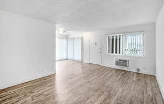 the living room and dining room of an apartment with white walls and wood flooring