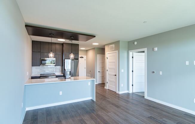 an empty living room with a kitchen and a door to a hallway