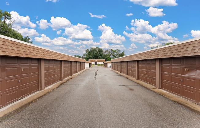 A long, narrow road flanked by brown garage doors under a blue sky with clouds.