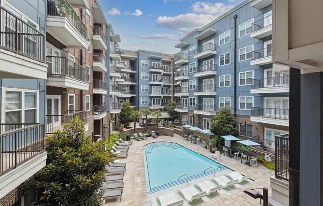 an outdoor pool with lounge chairs and umbrellas in front of an apartment building