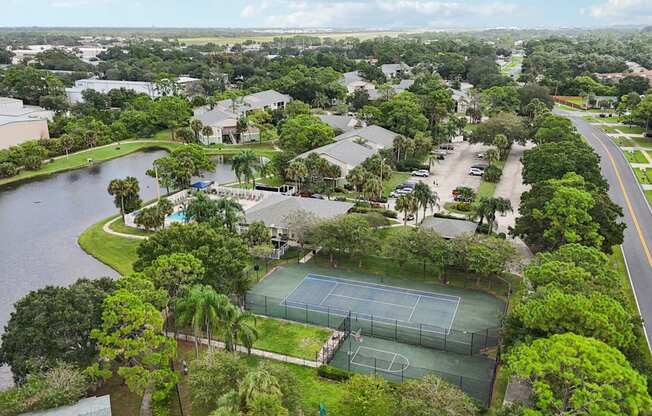 A tennis court is surrounded by trees and a body of water.