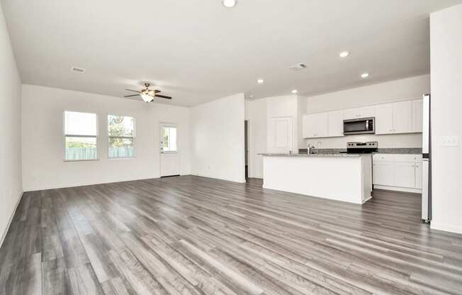 A spacious kitchen and living room with wood flooring and white walls.