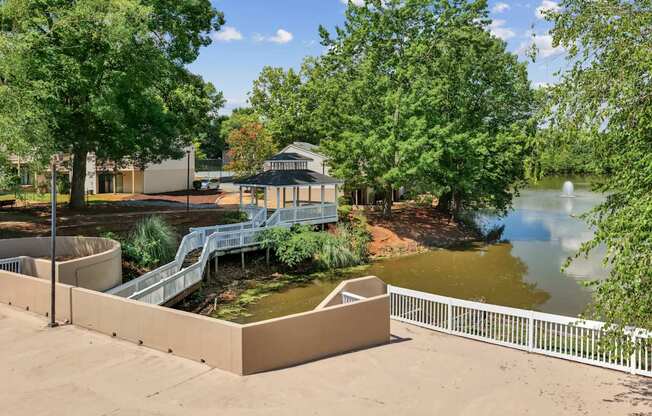 A gazebo sits in the middle of a park with a pond and a bridge.