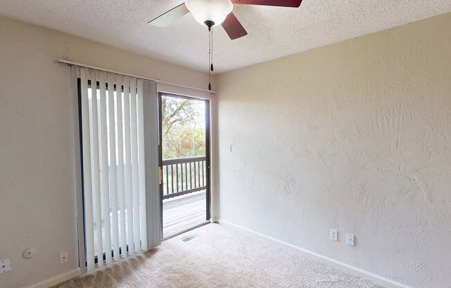 an empty living room with a ceiling fan and a door to a balcony