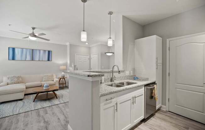 A modern kitchen with a white color scheme and a living room area with a sofa and a table.