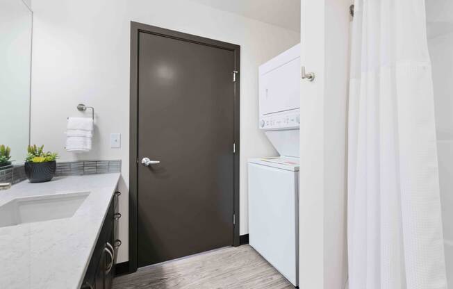 Greenwood, WA Apartments - The Morrow - Bathroom With In-Unit Washer And Dryer, Vinyl Plank Flooring, Granite Countertop, And Dark Brown Cabinets