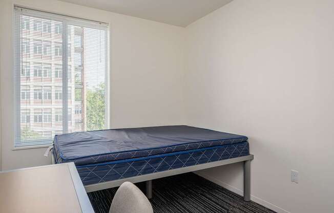 A bed with a blue mattress is in a room with a window.