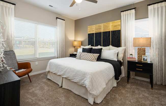 Furnished bedroom with queen size bed, two nightstands, carpet flooring, windows, and high ceiling at The Alexandria apartments in Madison, AL