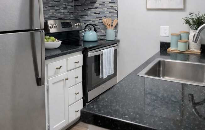 A modern kitchen with a black countertop and stainless steel appliances.