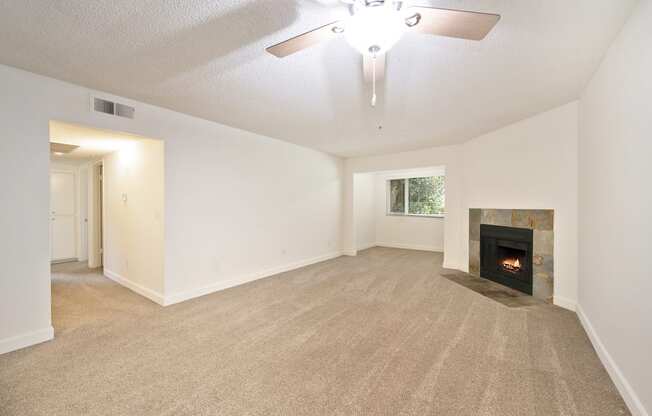 an empty living room with a fireplace and a ceiling fan