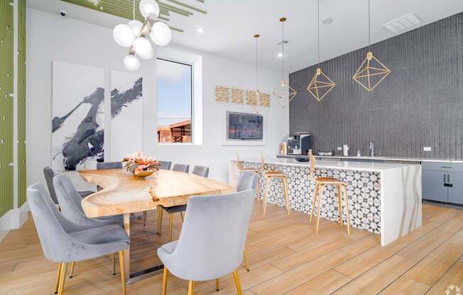 A modern community kitchen and dining room with a wooden table and grey chairs.