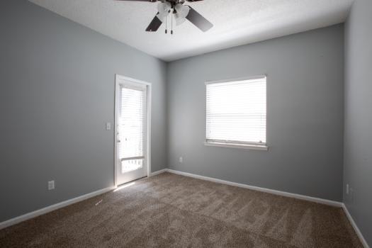 A room with a ceiling fan and two windows.
