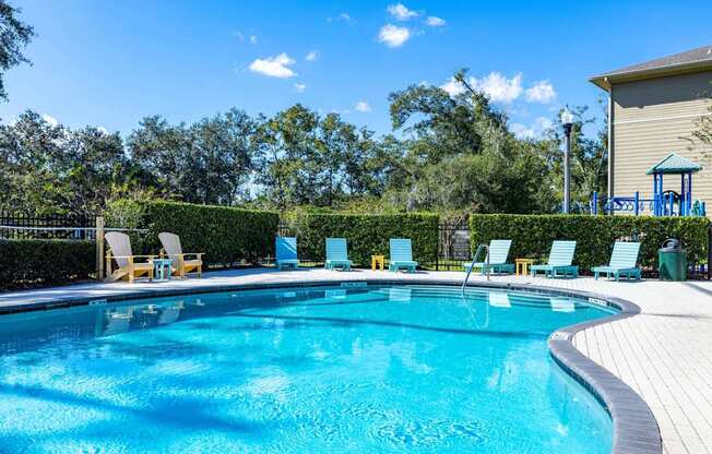 A swimming pool surrounded by trees and chairs.