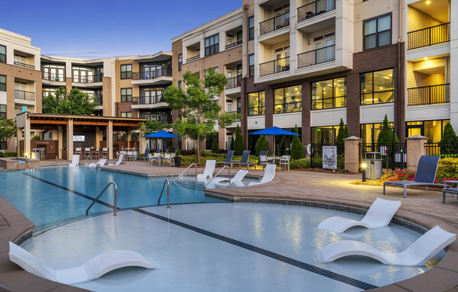 a swimming pool with lounge chairs in front of an apartment building