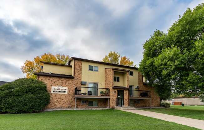 An apartment building with a green yard and a cloudy sky.Fargo, ND Huntington Apartments.