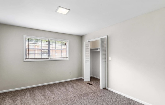 an empty bedroom with a window and a closet