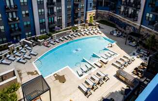 a large swimming pool with chaise lounge chairs and an apartment building in the background