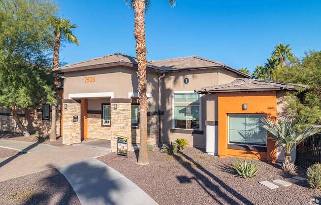A house with a brown roof and a yellow door is surrounded by palm trees.