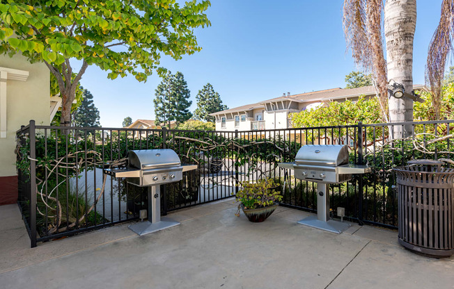 two bbq pits on a patio in front of a fence