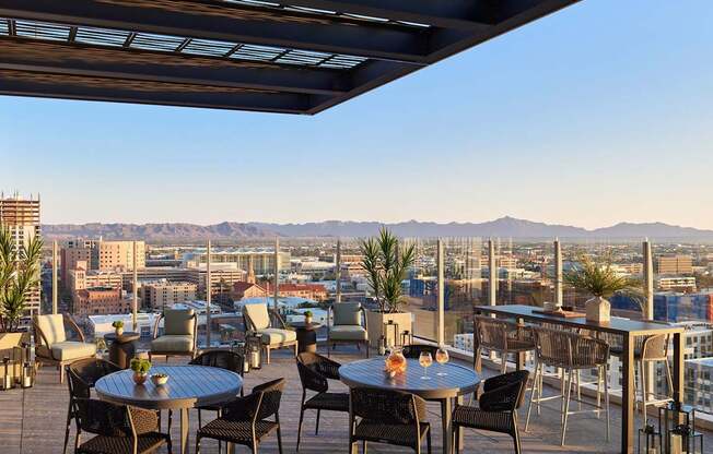 A rooftop patio with tables and chairs overlooking a cityscape.
