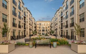 A courtyard with a bench and flower pots in front of apartment buildings.