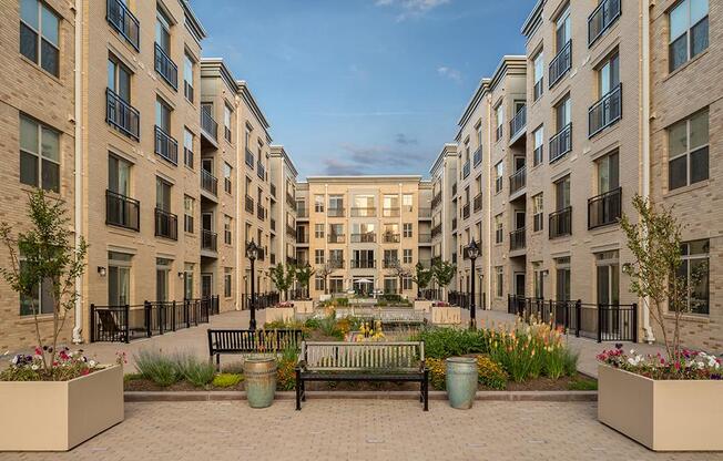 A courtyard with a bench and flower pots in front of apartment buildings.