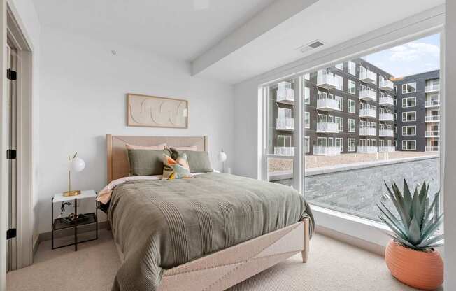 A bedroom with a large bed and a view of a building outside the window.