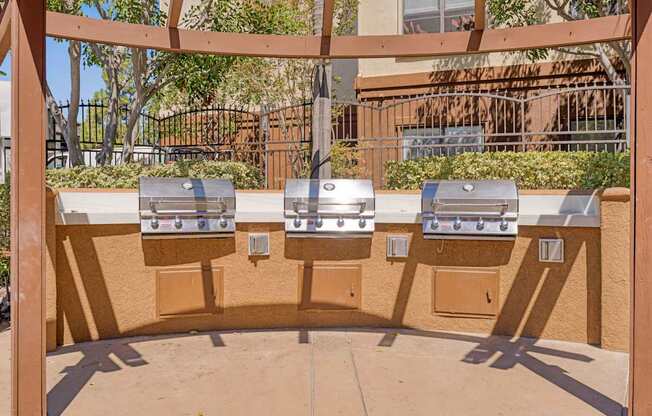 Three barbecue grills are lined up on a patio.