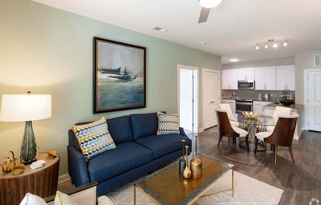 A living room with a blue couch and a painting of a boat on the wall.