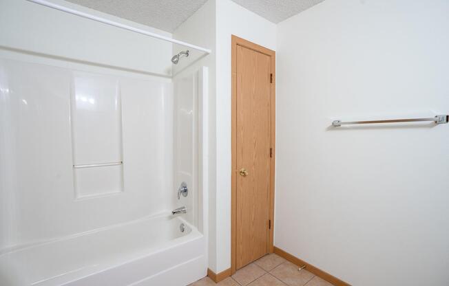 A white bathroom with a wooden door and a white bathtub. Bismarck, ND Sierra Ridge Apartments