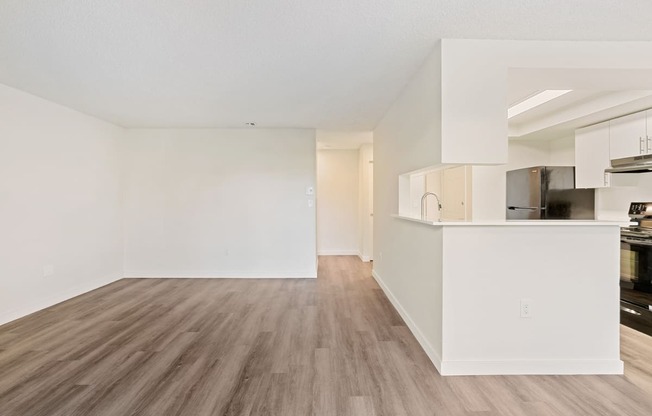 A spacious living room with wood flooring and the kitchen with a large breakfast bar to the right.