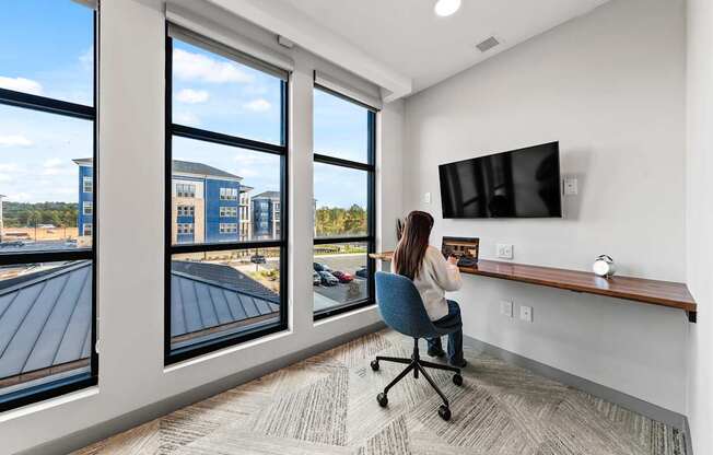 A woman is sitting at a desk in a private office with a large window at Preston Ridge Apartments Cary, NC.