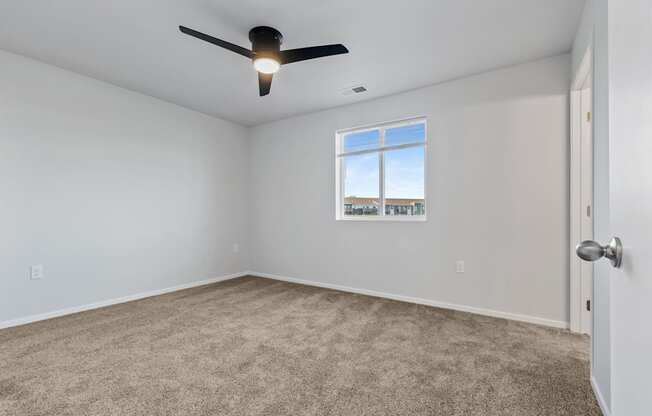 A room with a ceiling fan and a window showing a view of a building.